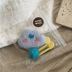 Close-up of handmade felt cloud hair clip and blue plush ball in zip packaging