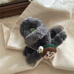 Détail d'une pince à cheveux en peluche grise avec personnage de fille sur fond en lin