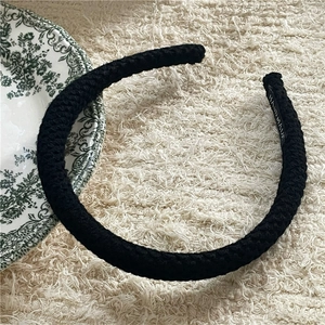 Detailed view of handmade black knitted headband with spiral texture on plush surface