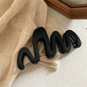 Vue détaillée d'une grande pince à cheveux noir mat ondulée sur un tissu en lin beige