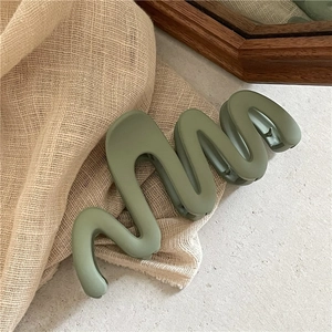 Détail d'une grande pince à cheveux mate verte au design ondulé sur un fond de tissu doux