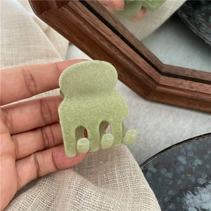 Dettaglio di una molletta per capelli verde chiaro floccata in mano con effetto velluto