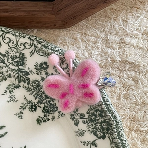 Détail macro d'une barrette papillon en peluche rose avec cristal de cœur et coutures douces