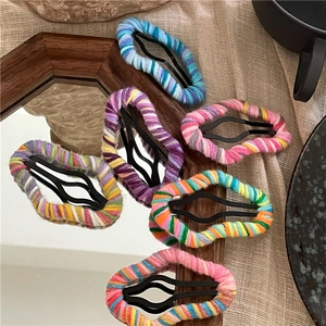 Close-up of six colorful wool-woven BB hair clips on a wooden mirror and beige fabric