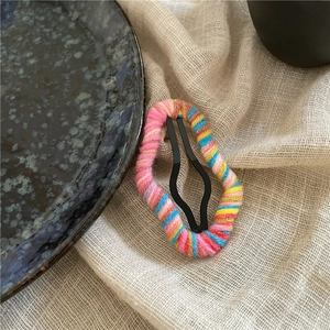 Detail showing colorful yarn wrapped around a hollow cloud hair clip on beige linen fabric
