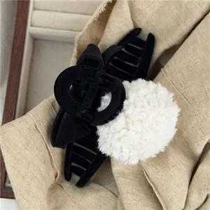Detail of a black velvet bow hair claw clip featuring a large white faux fur pompom