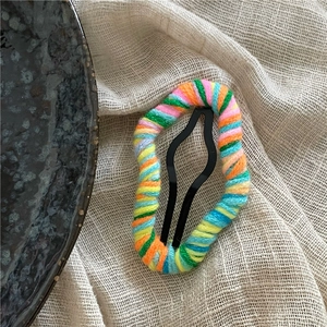 Detail shot of colorful yarn-wrapped cloud hair clip on a minimalist linen texture background
