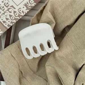 Detail of cream white matte hair claw clip on linen fabric with a 5-tooth resin design