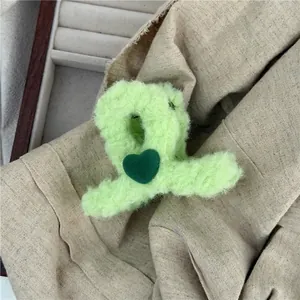 Detail of light green plush hair claw clip with dark green heart in woolly fabric texture