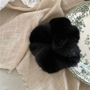 Detail of a black plush faux fur scrunchie resting on a rustic linen fabric background