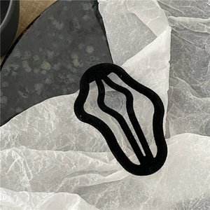 Detail shot of black flocked wave-shaped hair clip on marble and paper texture