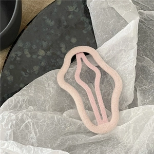 Close-up of a pink flocked wavy hair clip on a minimalist textured background