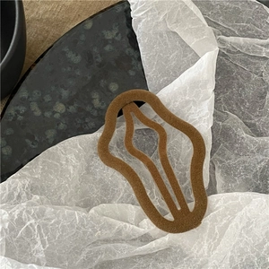 Close-up of brown flocked velvet hair clip with wavy hollow design on a ceramic plate