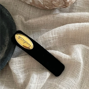 Macro detail of black flocked rectangular hair clip with golden Handmade metal label
