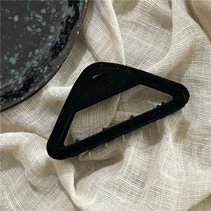 Close-up of a matte black flocked triangular hair claw clip on a minimalist textured background