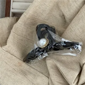 Macro shot of large black acrylic hair claw clip with faux pearl detail in packaging