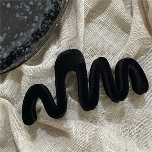 Close-up of black flocked hair claw clip with a wavy design on beige linen fabric