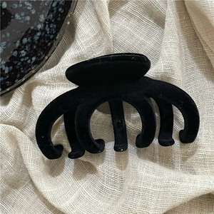 Close-up of large black flocked hair claw clip with multi-tooth design on white fabric