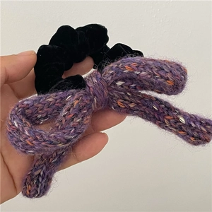 Detail view of black velvet scrunchie featuring a large colorful knitted wool bow accessory