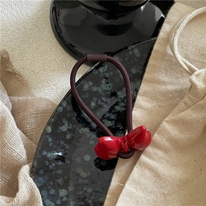 Detailed close-up of a glossy red bow hair tie placed on a rustic linen cloth and stone