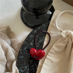 Close-up of a glossy red heart charm with a brown elastic hair tie on a ceramic display