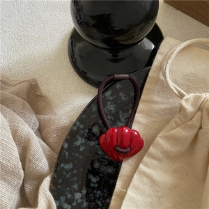 Detail of red shell-shaped resin hair tie with a durable elastic band on a ceramic tray