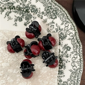 Mini mollette per capelli con perle rosse e base nera su un piatto con motivi floreali