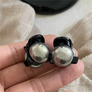 Dettaglio macro di due mini fermagli per capelli con perle grigio argento e base nera lucida