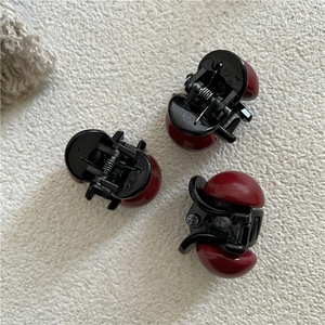 Dettaglio di mini mollette per capelli con perle rosse e resina nera su tessuto a trama