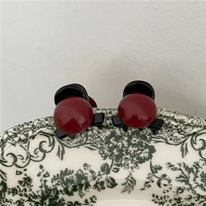 Dettaglio di mini mollette per capelli rosse e nere su un piatto di ceramica floreale