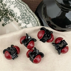 Dettaglio di cinque mini mollette per capelli con perle rosse su fondo in tessuto beige