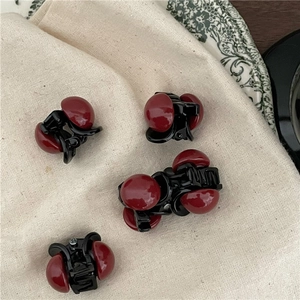 Dettaglio di quattro mini mollette per capelli con perle rosse su tessuto di lino