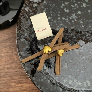 Détail de l'élastique à cheveux noir avec ruban en daim marron et deux coeurs dorés en métal
