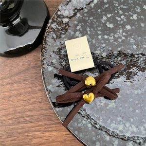 Détail de chouchous en velours marron avec breloques cœur doré sur carte de présentation