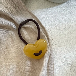 Gros plan d'un chouchou avec perle de cœur jaune sur un fond en tissu beige texturé