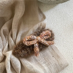 Détail de la pince à cheveux en peluche marron ornée d'un nœud en laine tricoté pêche