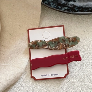 Vue détaillée de barrettes ondulées en acétate vert marbré et rouge avec logo doré