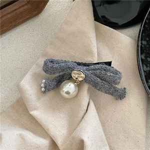 Detailed macro view of gray knitted bow hair clip with white pearls and gold accents
