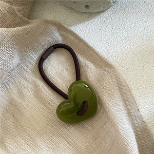 Gros plan de perles en forme de cœur vert herbe sur un élastique à cheveux marron foncé