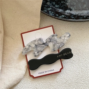 Détails de barrettes à cheveux ondulées en acétate avec logo doré sur carte de présentation