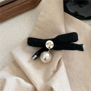 Detail of wool bow hair clip with gold logo medal and large hanging faux pearl drop