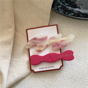 Détail de barrettes ondulées en acétate avec texture marbrée rose et lettres dorées