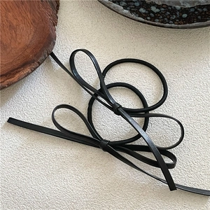 Detail of two minimalist black PU leather bow hair ties on a textured white surface