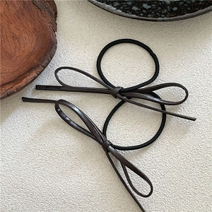 Close-up of two dark brown PU leather bow hair ties with elastic black bands