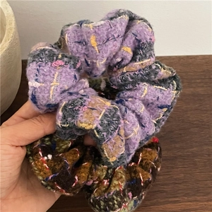 Hand holding two thick tweed plaid hair scrunchies in lilac and caramel brown colors