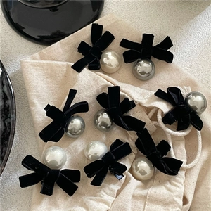 Detailed view of black velvet bow hair clips with large faux pearl beads on burlap fabric