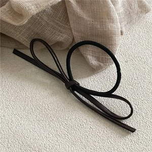 Close-up of a deep brown PU leather bow hair tie with a black elastic band on fabric