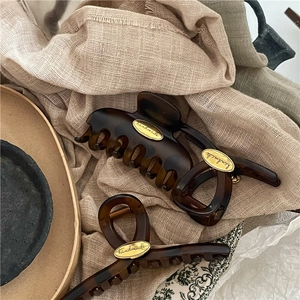 Macro detail of tortoiseshell hair claw clips with handmade metal tag on soft linen fabric