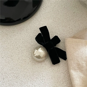Close-up of black velvet bow hair clip featuring a large faux pearl on a textured surface