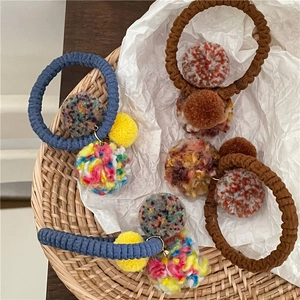 Detailed view of colorful knit pom-pom hair ties on white paper inside a woven basket
